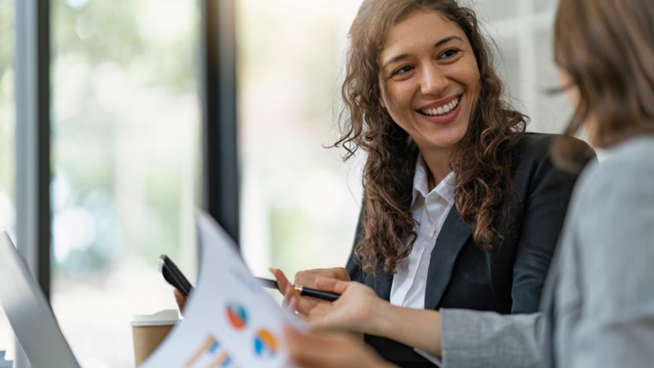 two business women talk to each other while looking at paperwork