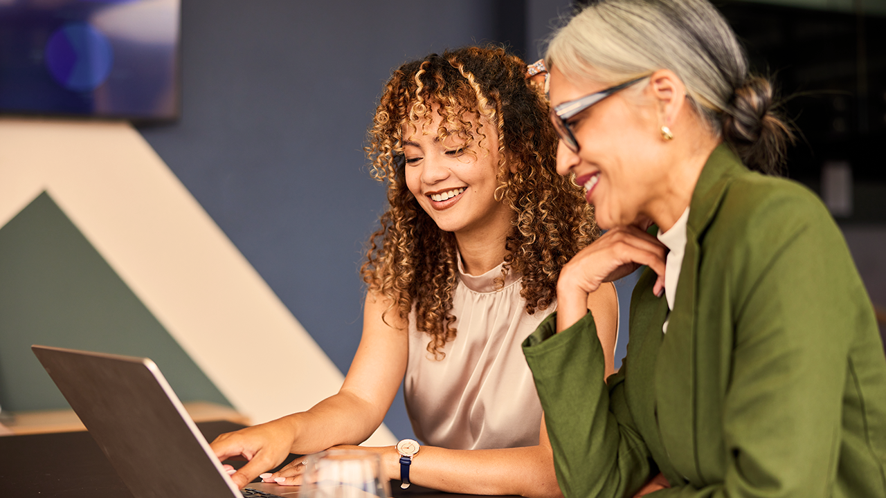 Two women smiling and collaborating over a laptop in an office