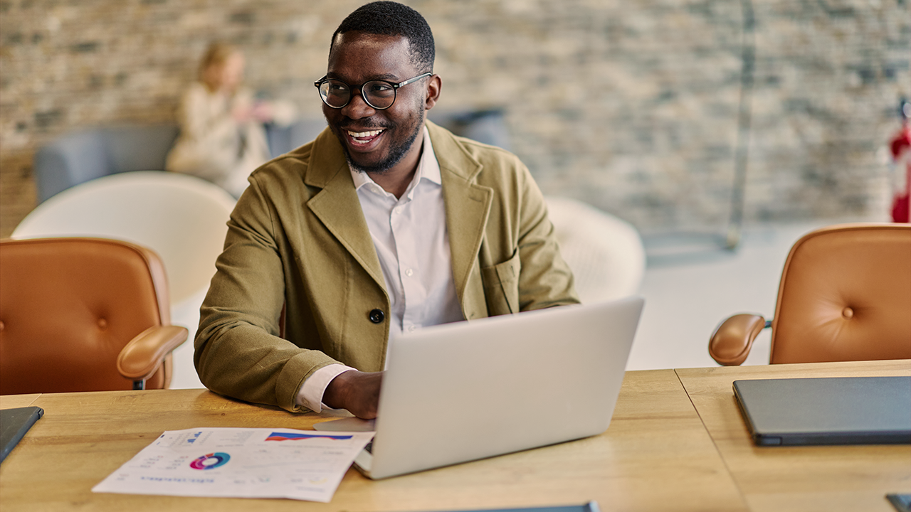 Smiling man in blazer working on laptop at office table with charts