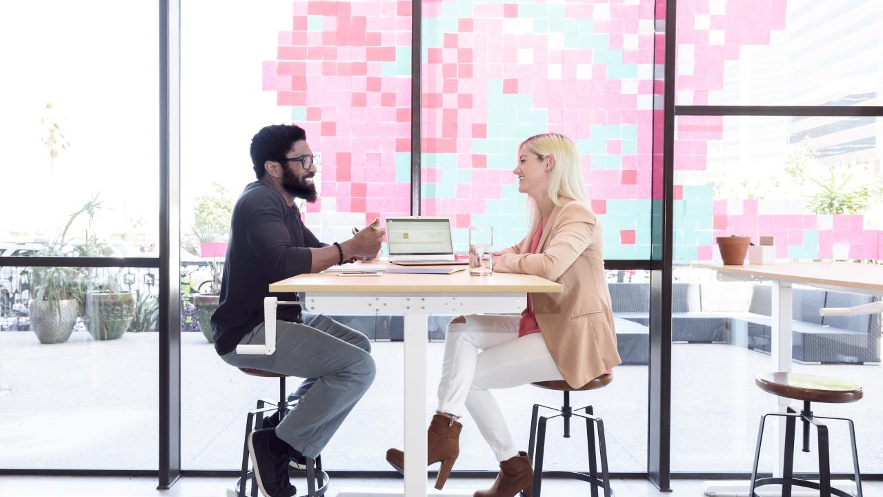 A man and woman sit at a cafe table talking.