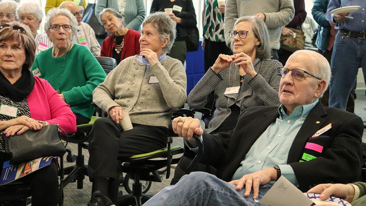 A group of older adults sitting in a circle, engaged and listening attentively.
