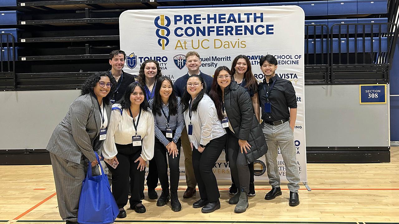Students smiling in gym before Pre-Health Conference banner (photo)