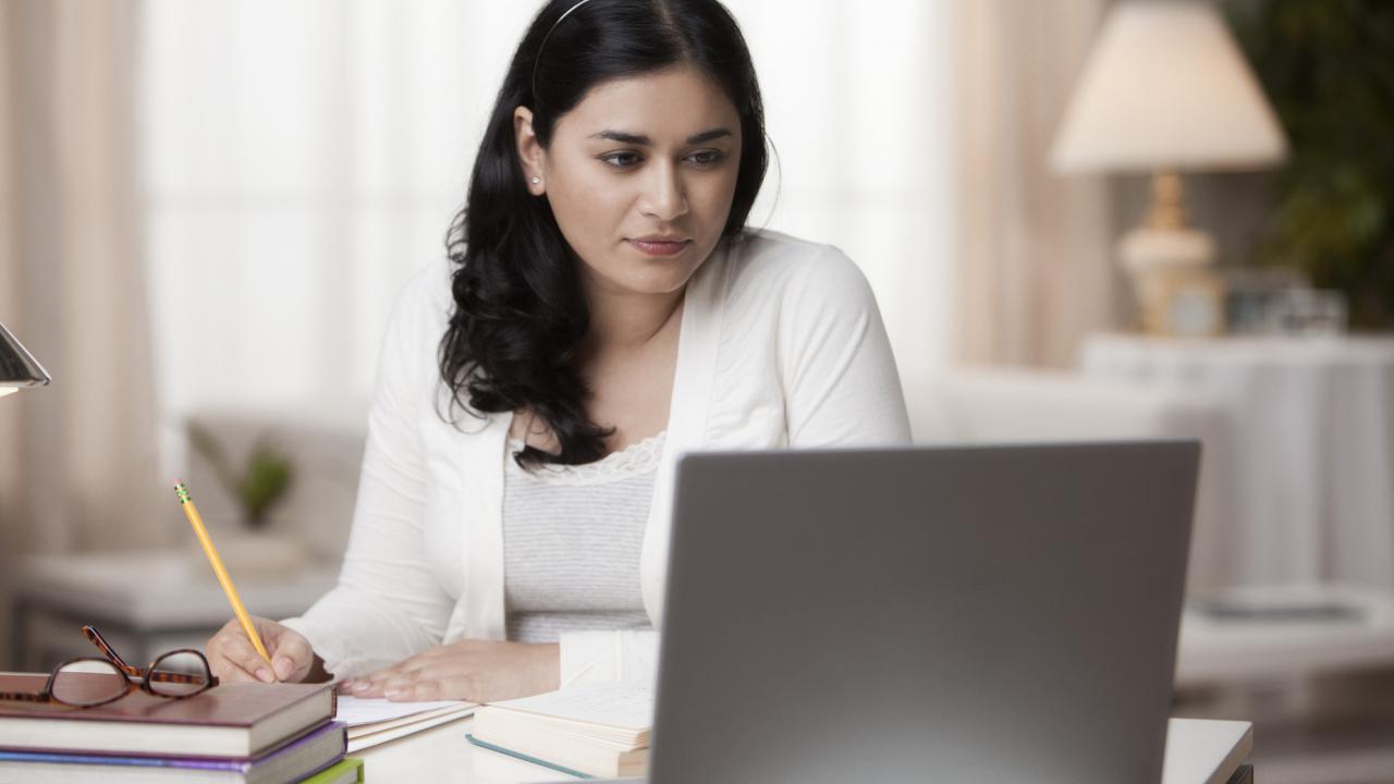 A woman with a pencil reviewing information on a laptop screen.