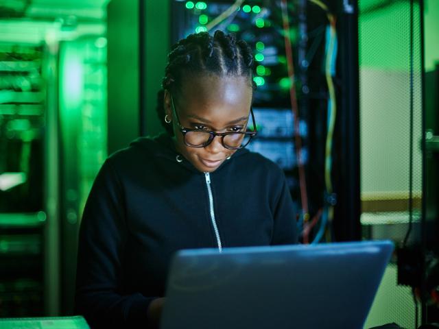 female computer programmer sitting at laptop in dark server room