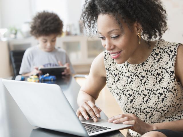 mom on laptop with son in background on tablet