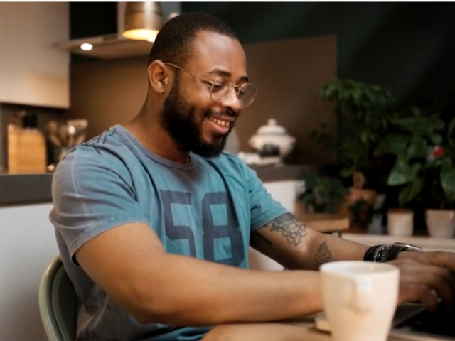 A man at a table with coffee and a computer, smiling