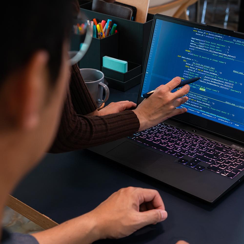 woman pointing out some code on a laptop screen as a student looks on
