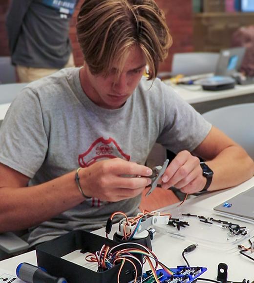 Young man concentrating, using tweezers to assemble electronic circuit with wires and laptop