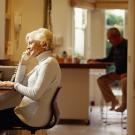 Senior woman using computer and telephone, senior man in background 