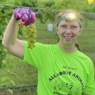 UC Davis Winemaking Certificate graduate Ann Kane poses in her vineyard holding a bunch of grapes with headlamp on