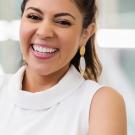 Woman with white clothing and dark hair smiling with a blurred background