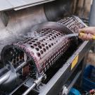 Hand of worker washing crushing machinery from hose at winery