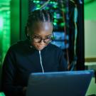 female computer programmer sitting at laptop in dark server room