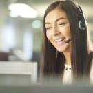 a woman with a phone headset on smiles while talking 