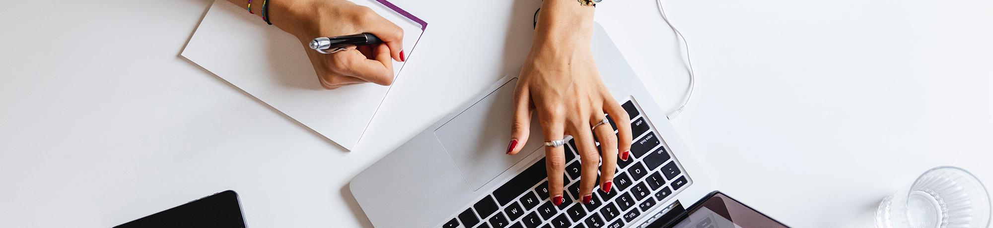 woman taking notes on an online class with a laptop