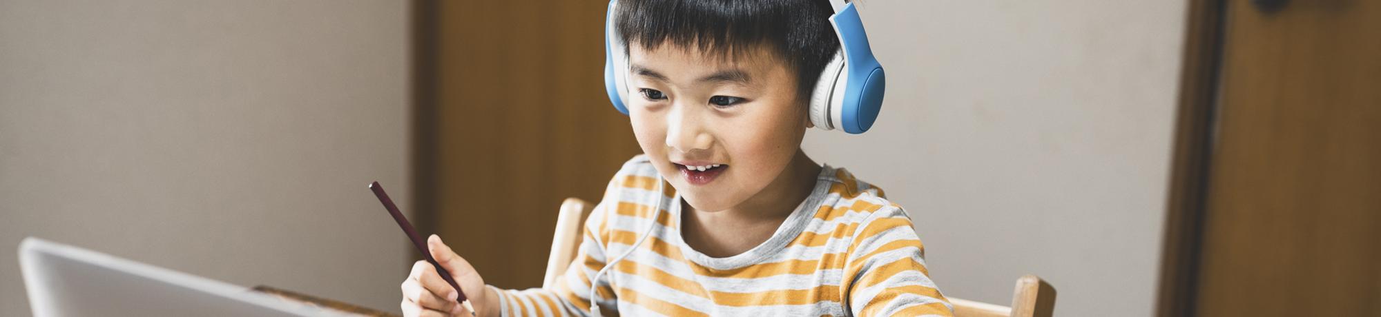 boy working at desk wearing headphones looking at laptop computer