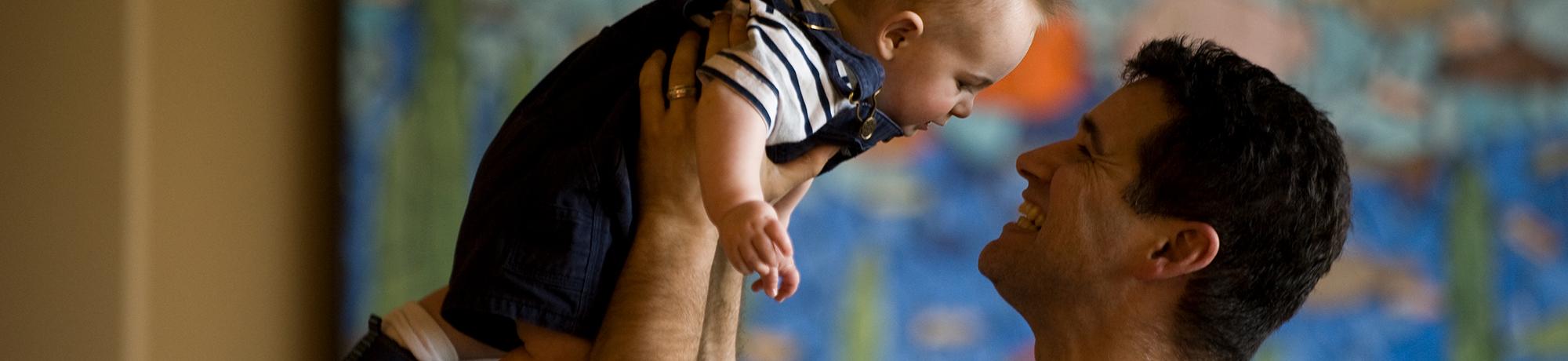 man holding smiling baby above his head
